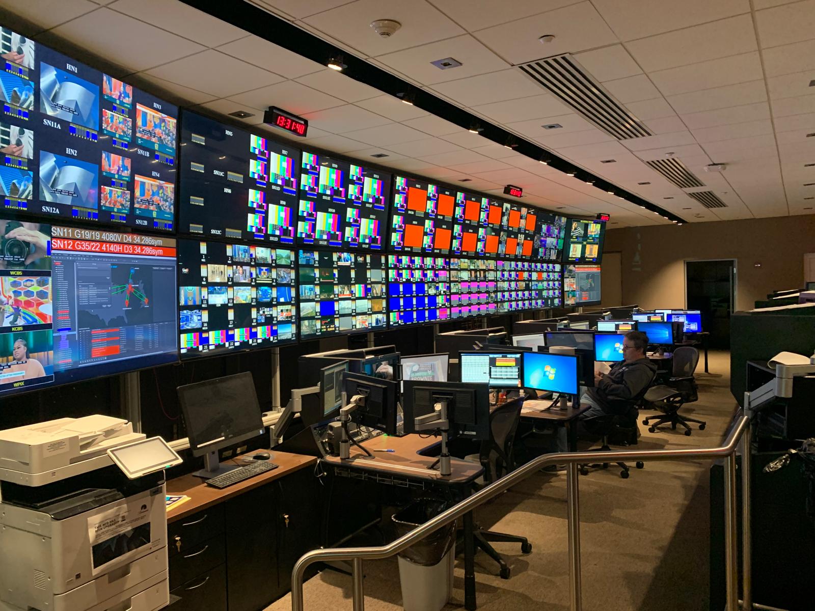 CBS control room with a large wall of live broadcast feeds and operator workstations.